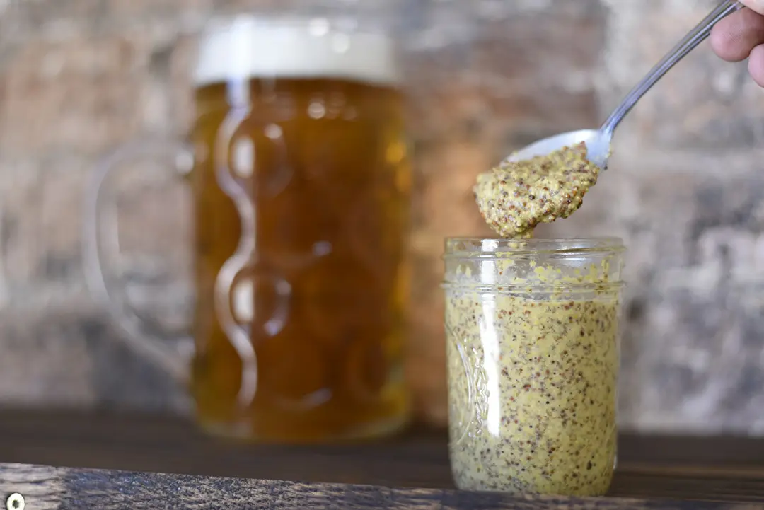Spoonful of mustard with beer mug behind.