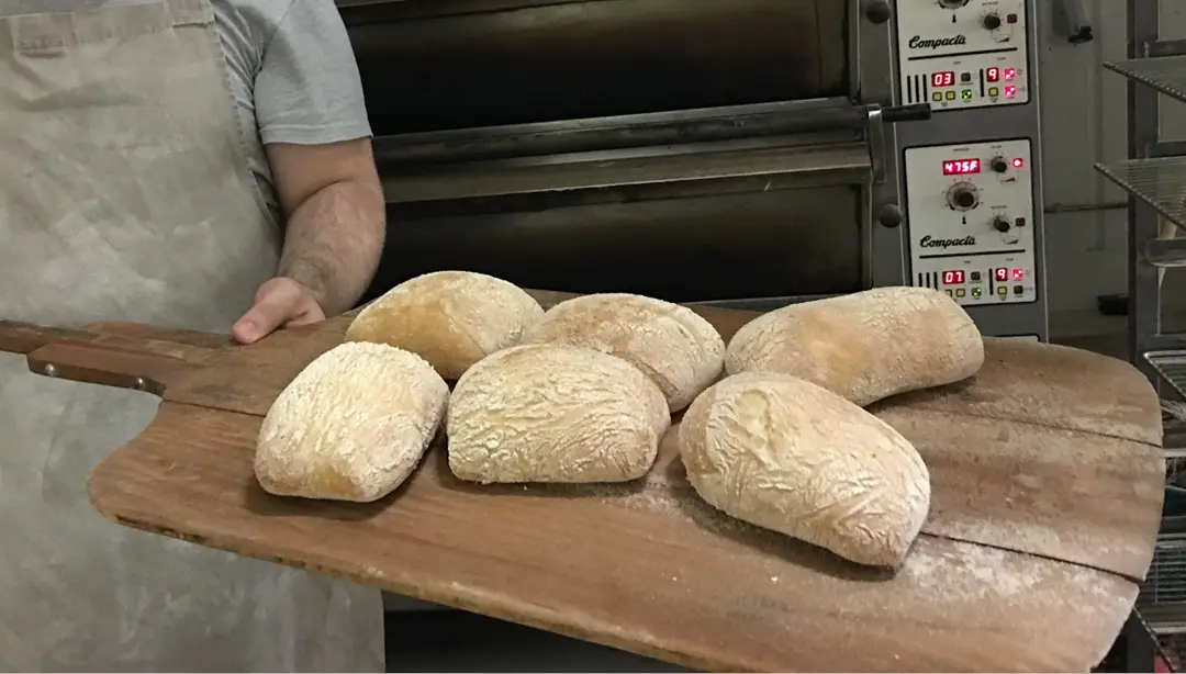 Baker holding freshly baked bread rolls.