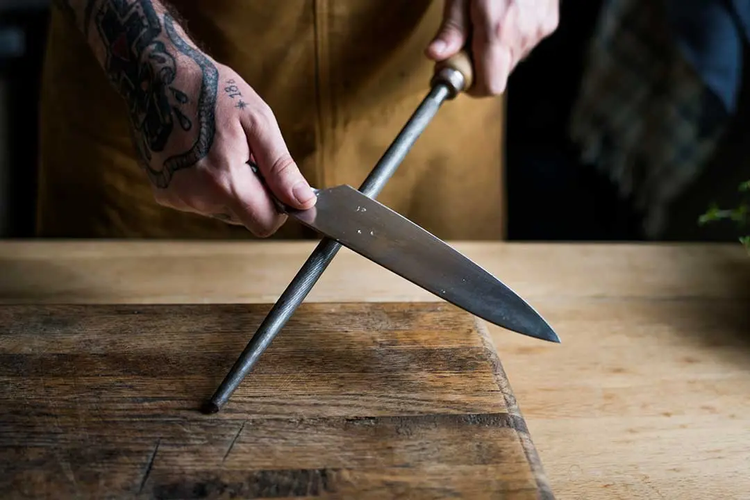 Hand honing a chef's knife with a sharpening steel, traditional kitchen tool essential for Mediterranean cooking.