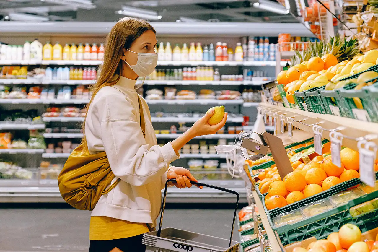 Woman shopping for fruit in supermarket, wearing mask.