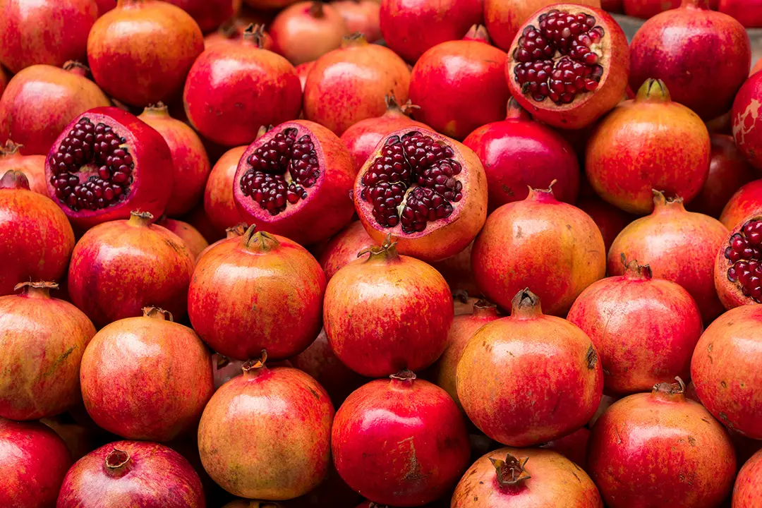 Fresh pomegranates, some halved, in a market.