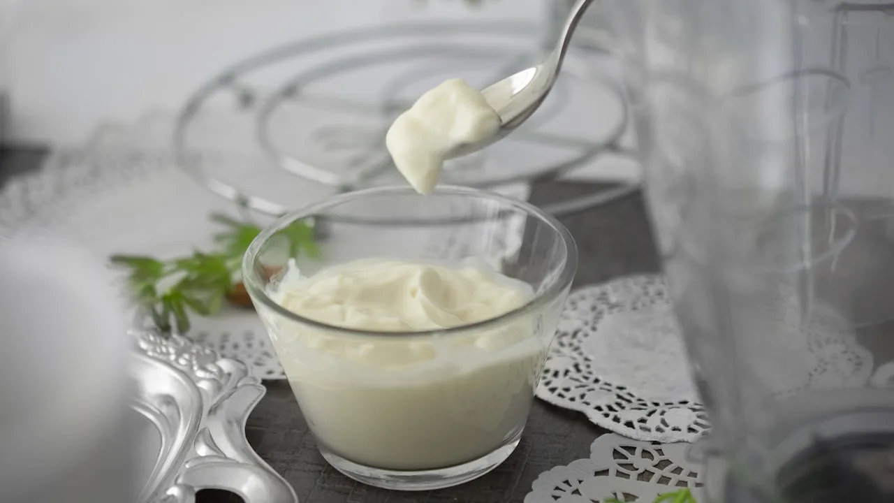 Spoon lifting creamy mayonnaise from glass bowl